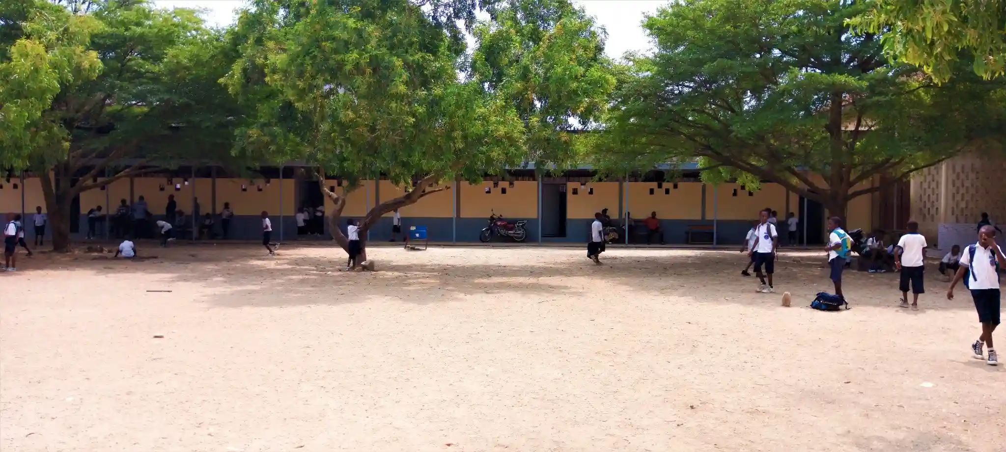 Élèves de primaire assis en classe écoutant un enseignant, pupitres et tableau noir en arrière plan, lumière naturelle par de grandes fenêtres, atmosphère studieuse et chaleureuse, pas de texte visible